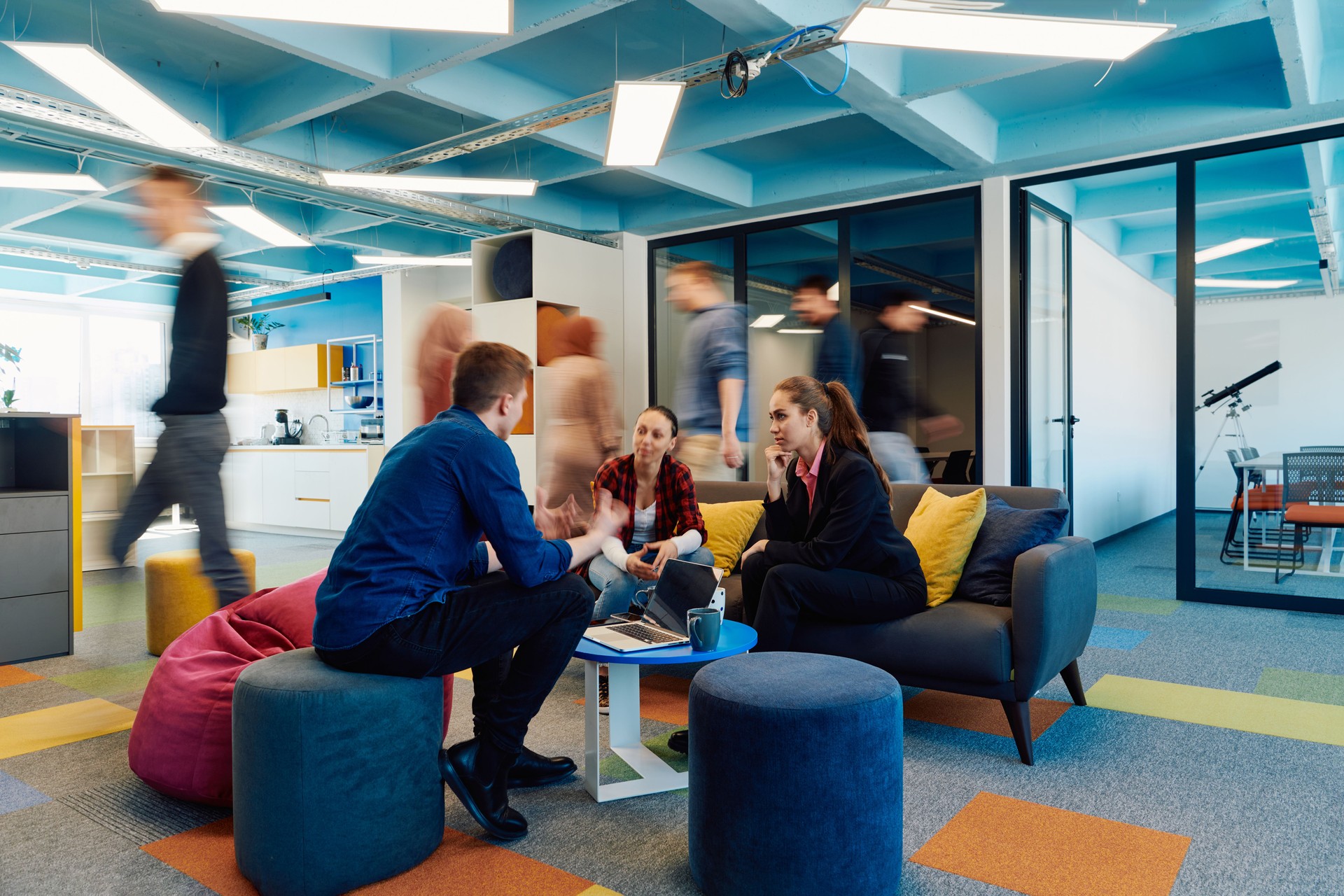 Multiethnic startup business team on meeting in a modern bright open space coworking office. Brainstorming, working on laptop. Group of coworkers walking around in motion blur